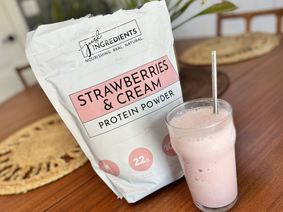 A bag and a glass of of Just Ingredients Strawberries & Cream Protein Powder