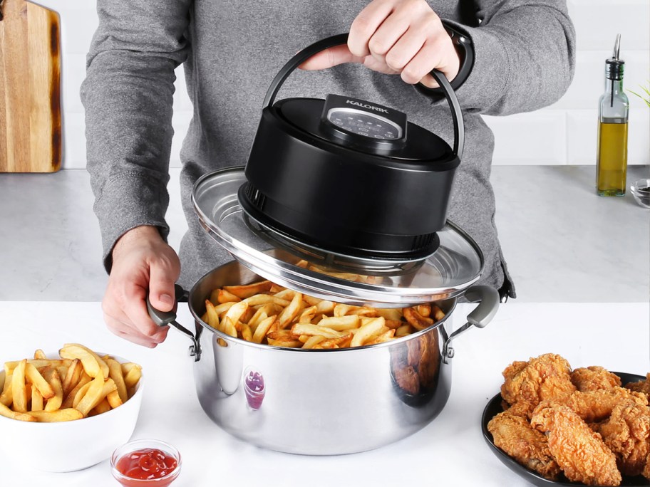 person removing air fryer lid from pot filed with french fries