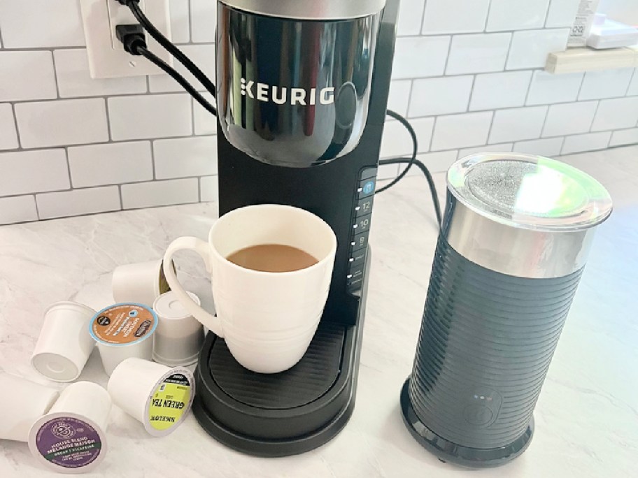 black keurig next to a black milk frother and a white coffee mug