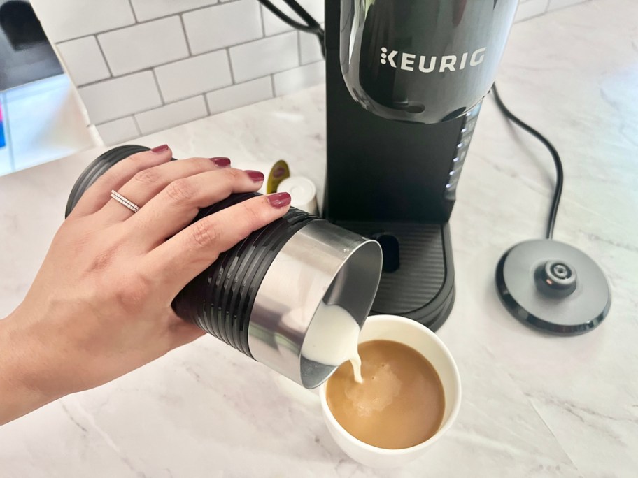 woman pouring milk from a frother in front of a Keurig K-Cafe Barista machine