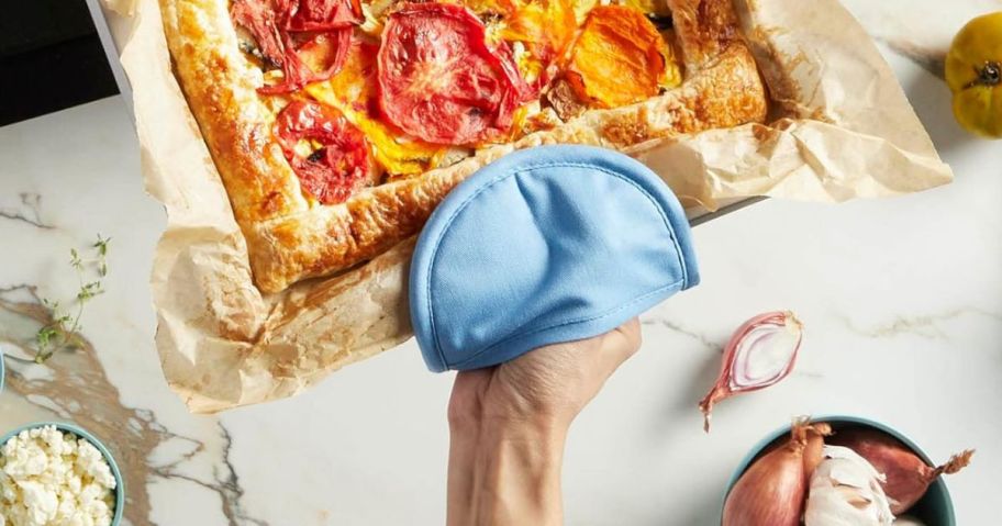 A person holding a pizza pan with a blue pot holder