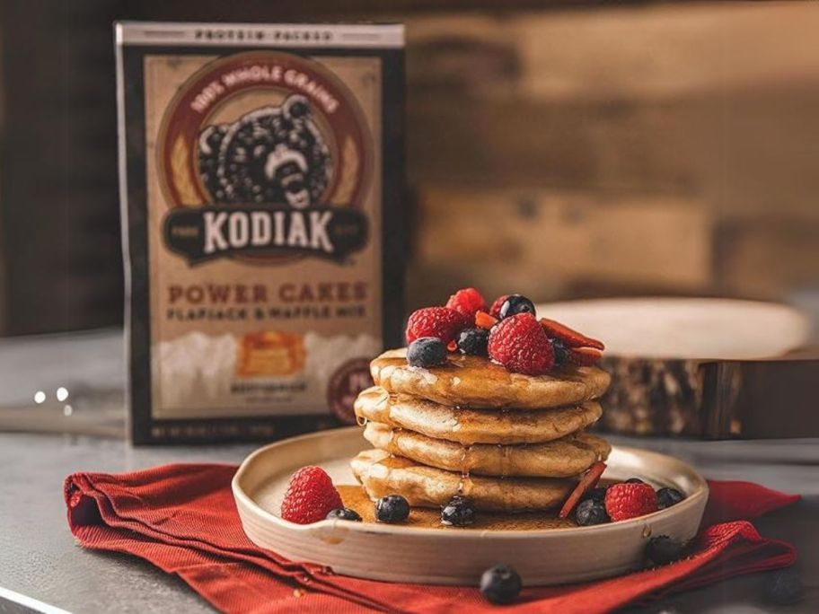 Kodiak Cakes Protein Pancake Power Cakes, Flapjack and Waffle Baking Mix, Buttermilk, 20 Oz box with pancakes and berries stacked in front of it