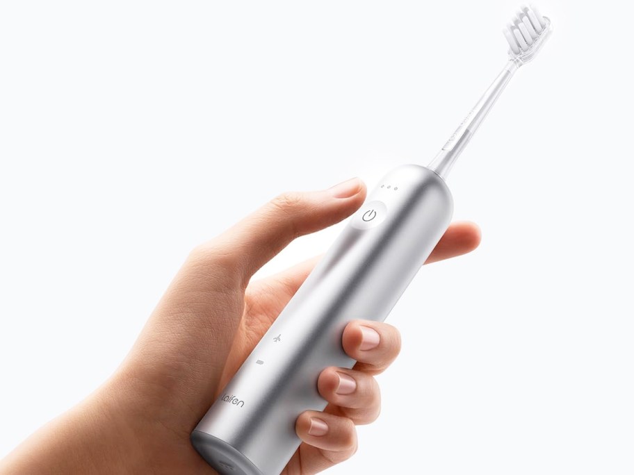 hand holding a silver electric toothbrush