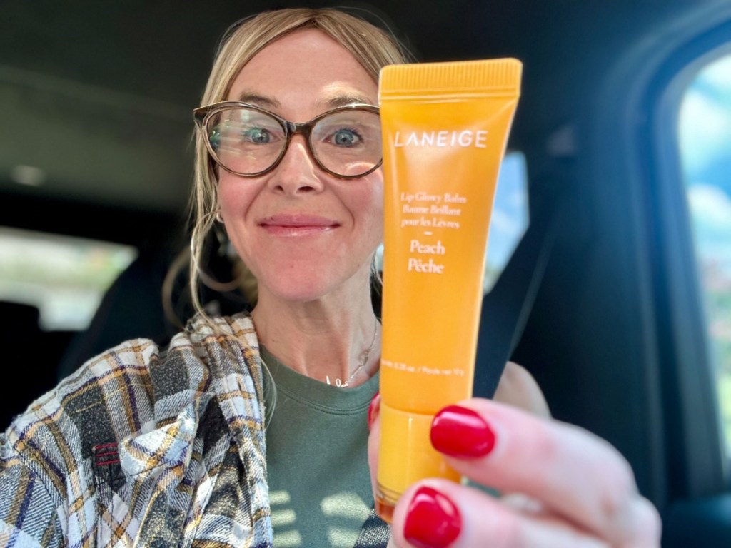 woman holding up peach Laneige Lip Balm in car