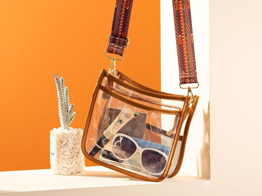 clear crossbody bag holding sunglasses and accessories