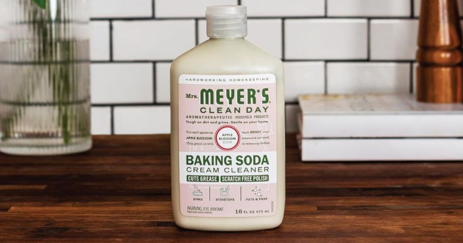 A bottle of Mrs Meyer's Clean Day Baking Soda Cream Cleaner on a wood counter