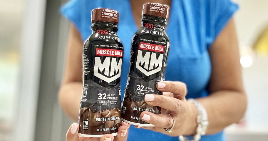 woman in blue shirt holding up two bottles of Muscle Milk