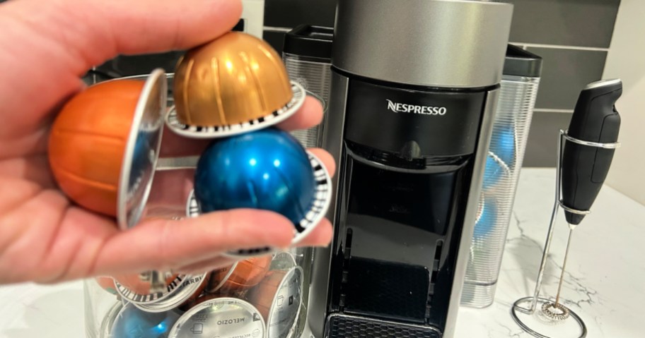 person holding nespresso pods in front of nespresso machine