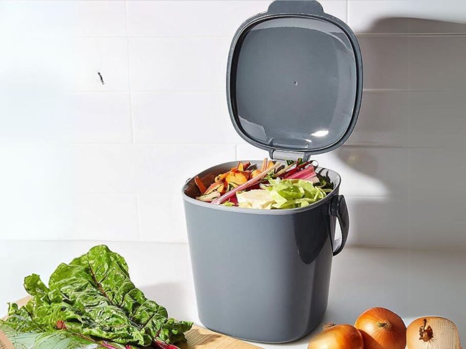 OXO Good Grips Easy-Clean Compost Bin in Charcoal on counter with compost in it and vegetables laying around it