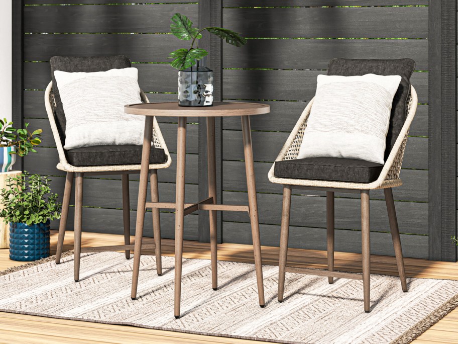 wicker patio chairs with black cushions and white pillows and tall dining table