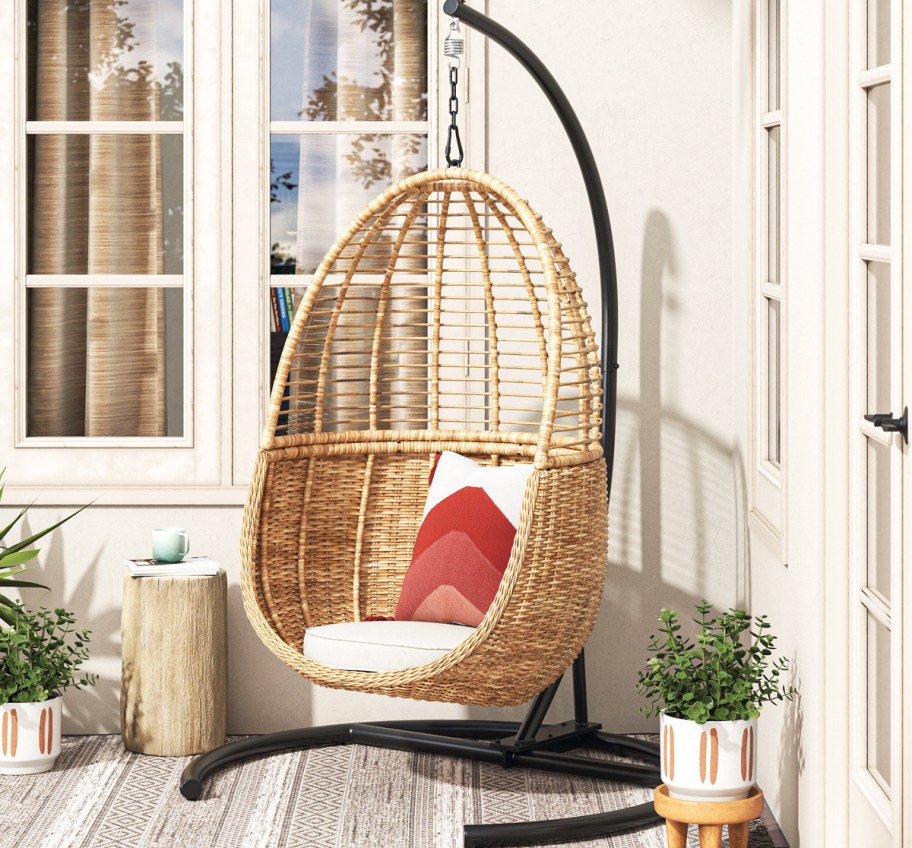 wicker hanging egg chair with white cushion and red throw pillow
