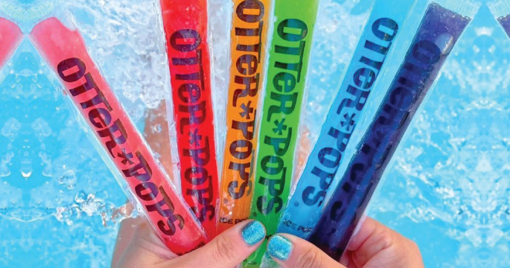 person holding up otter pops in front of blue water