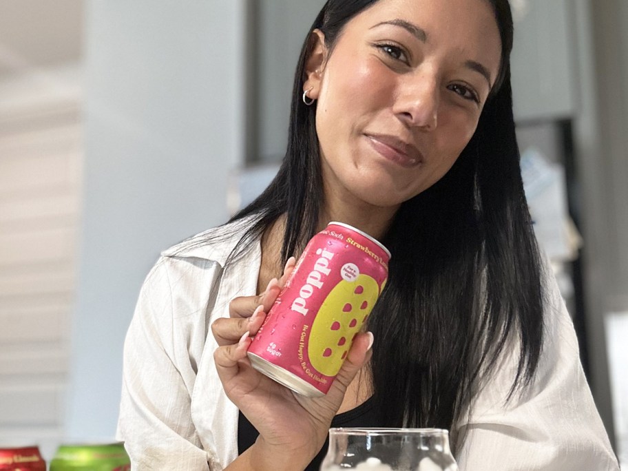 woman holding up a pink can of poppi soda