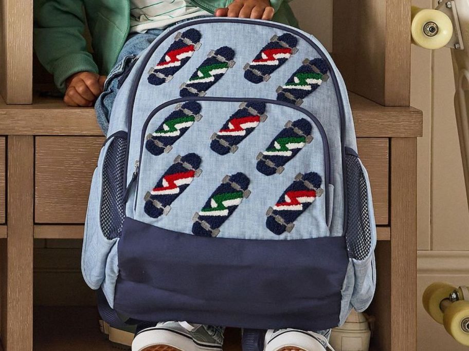 A boy holding a Pottery Barn Kids Mackenzie Chenille Skateboards Backpack