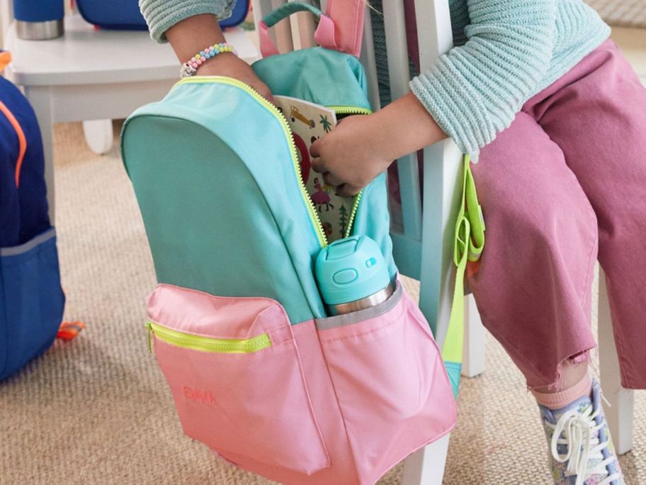 girl reaching into a pottery barn backpack hanging on the back of a chair
