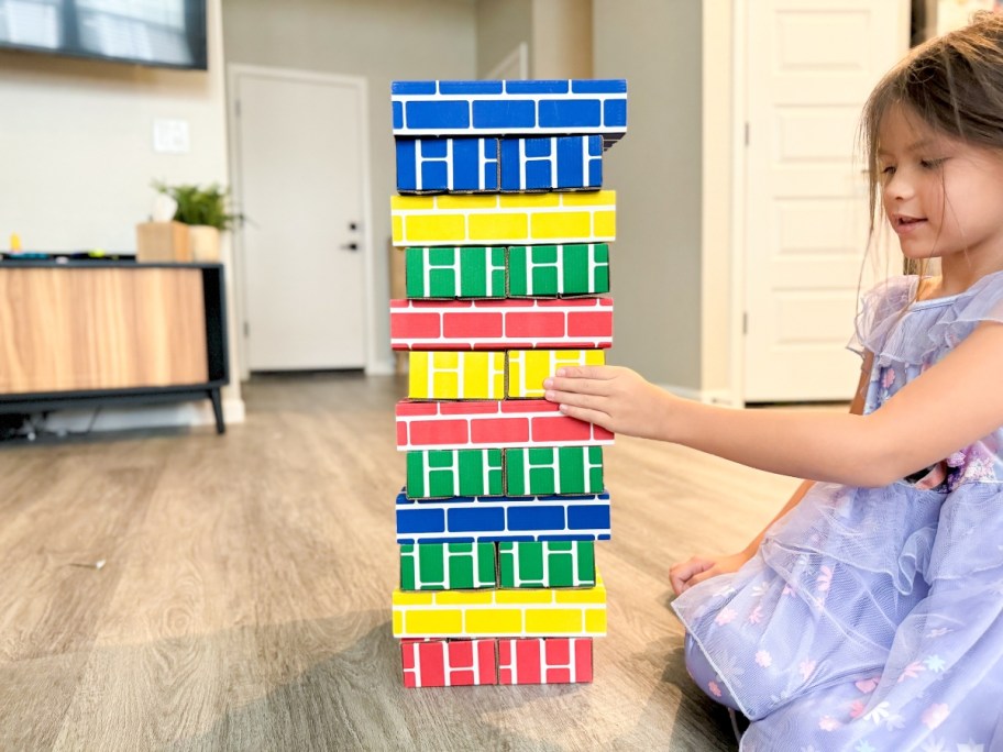 little girl playing with a tower made from primary color cardboard building blocks