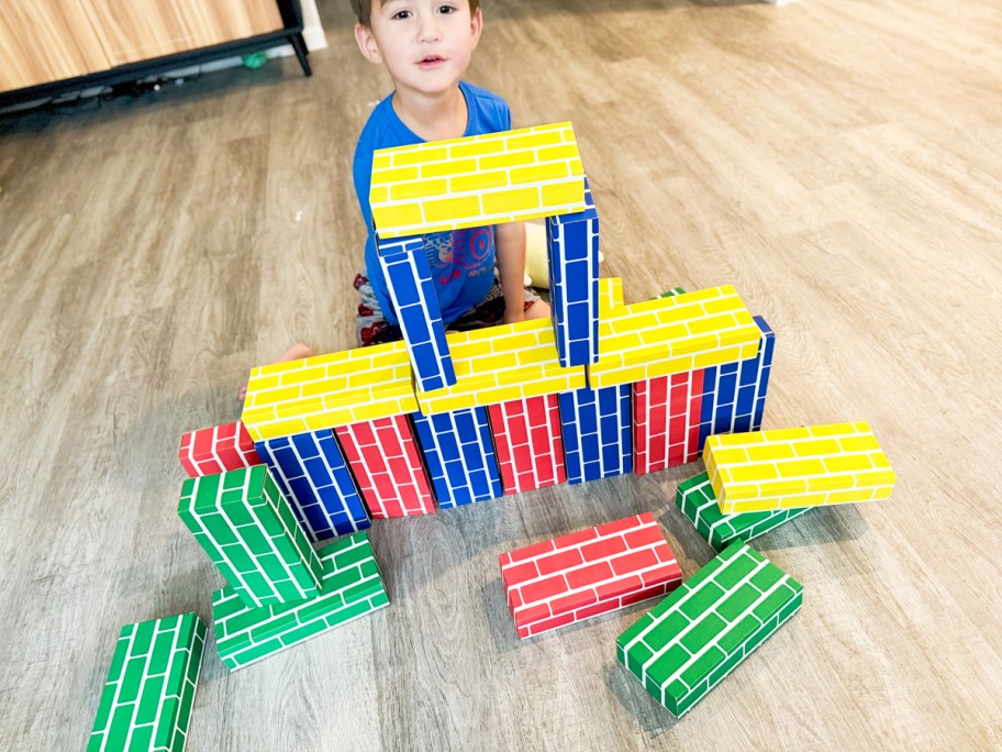 boy playing with colorful cardboard building bricks on floor