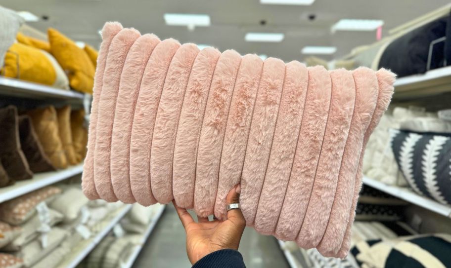a womans hand holding a pink faux fur lumbar throw pillow