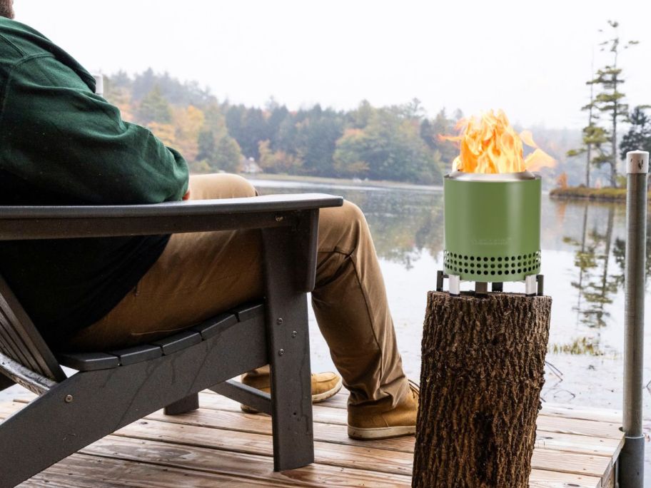 Solo Stove Mesa XL Fire Pit in Deep Olive by the lake on a tree stump