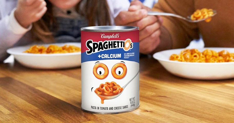 can of SpaghettiOs Original Plus Calcium on table with father and daughter eating some in background