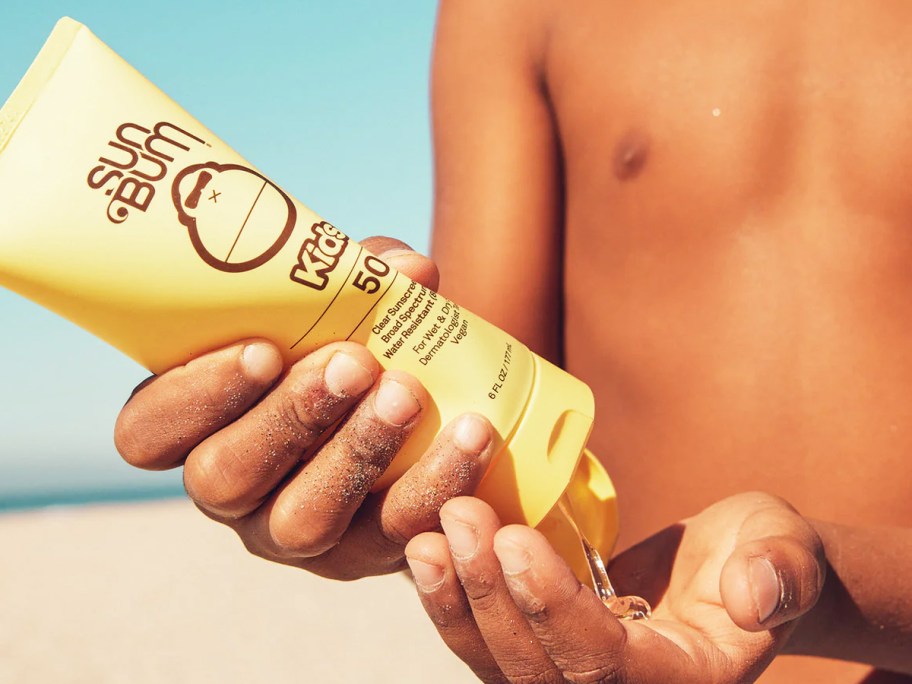 boy squeezing a tube of Sun Bum Kids SPF 50 Clear Sunscreen Lotion