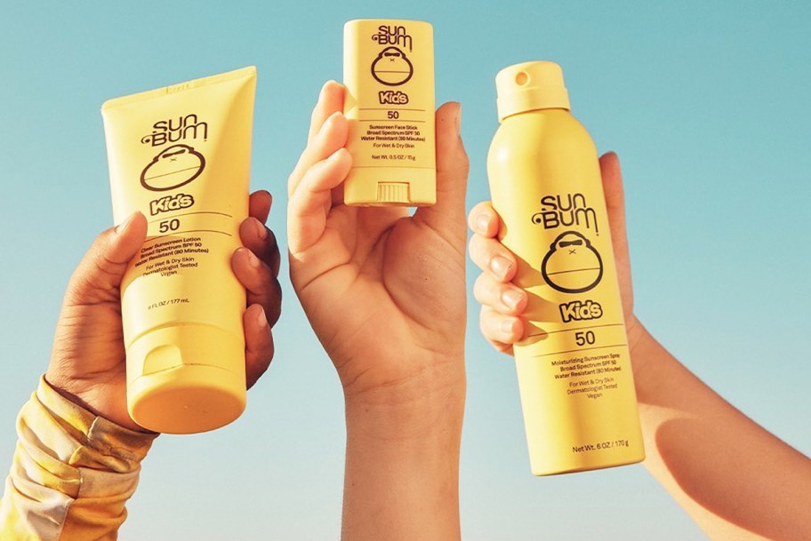three hands holding up yellow bottles of Sun Bum sunscreens
