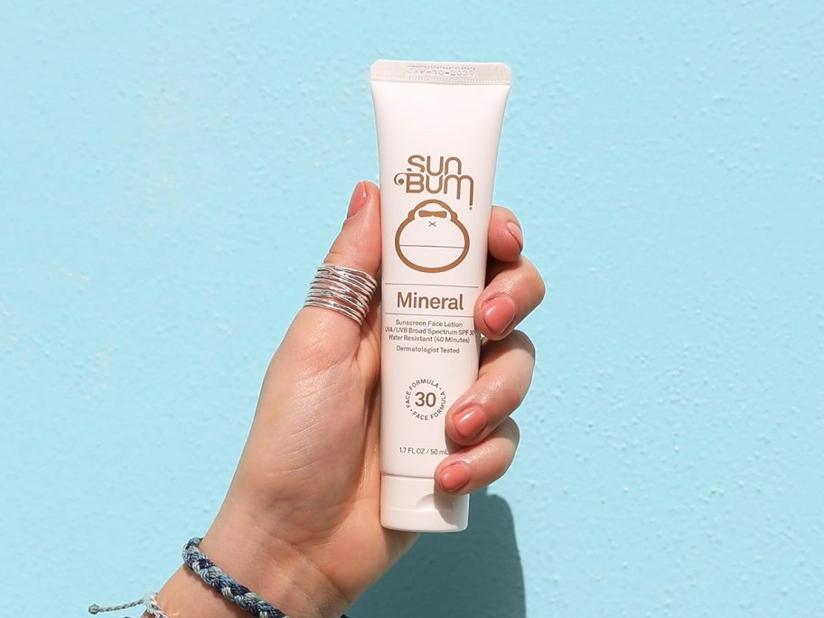 hand holding a white tube of Sun Bum Mineral Sunscreen Face Lotion
