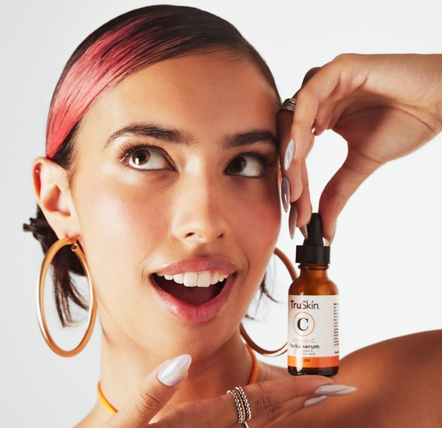 Woman holding a bottle of vitamin C serum to her face