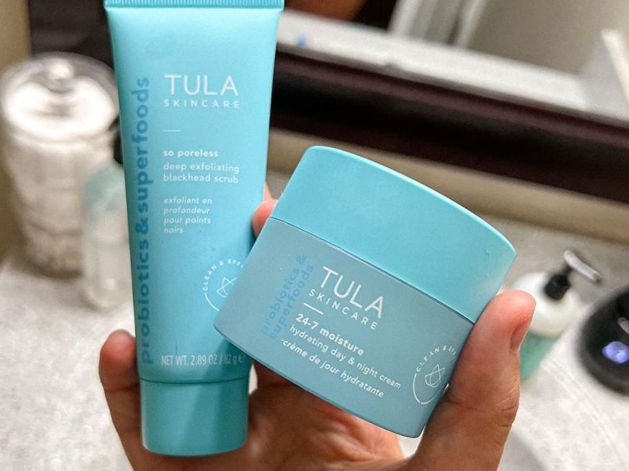 Hand holding a small Tula Cleanser and a jar of 24-7 Moisture Day & Night Cream