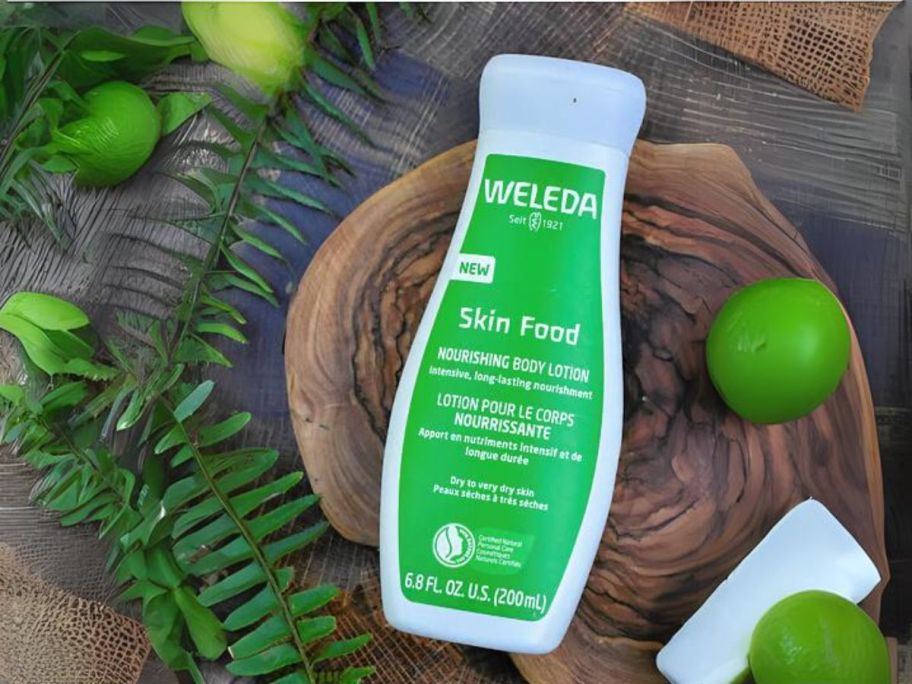 Weleda Skin Food Body Lotion 6.8oz bottle on bamboo tray with limes and leaves around it