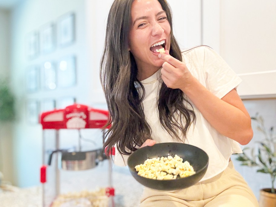 woman sitting on kitchen counter eating bowl of popcorn