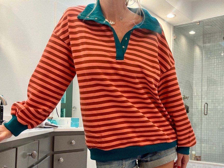 woman wearing a coral and orange striped sweatshirt that has a green collar and band around the sleeves and bottom