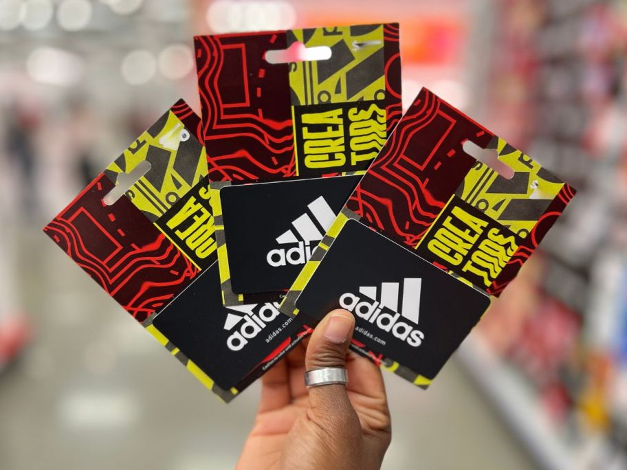 hand holding 3 adidas gift cards in store