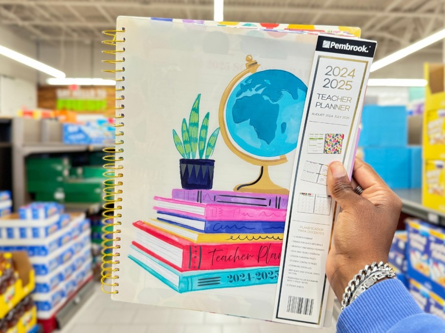 hand holding a teacher palnner with a globe and school books on the cover