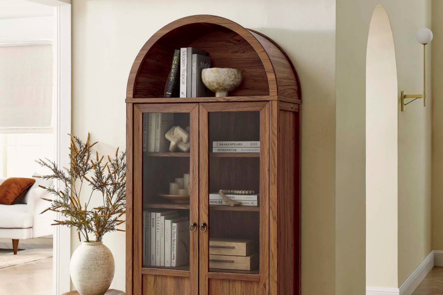 arched cabinet filled with decor pieces standing against a wall