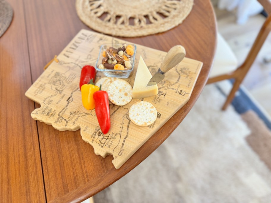 peppers, crackers, nuts and cheese on top of a bamboo state cutting board