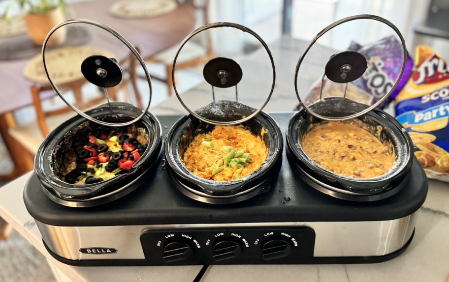 triple slow cooker with three different meals inside and lids hanging on side