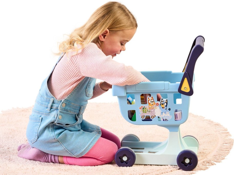 little girl reaching into a bluey shopping cart