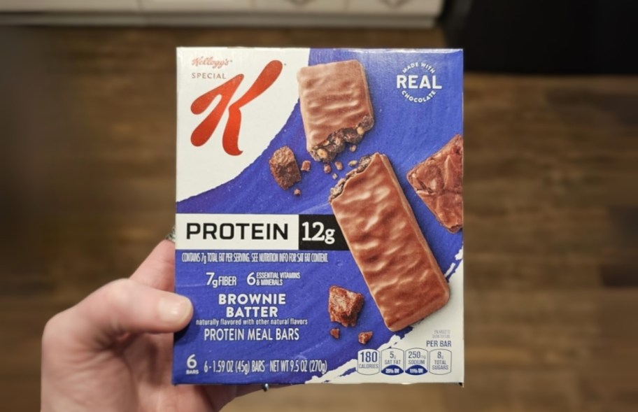 a man's hand holding a box of brownie batter protein bars