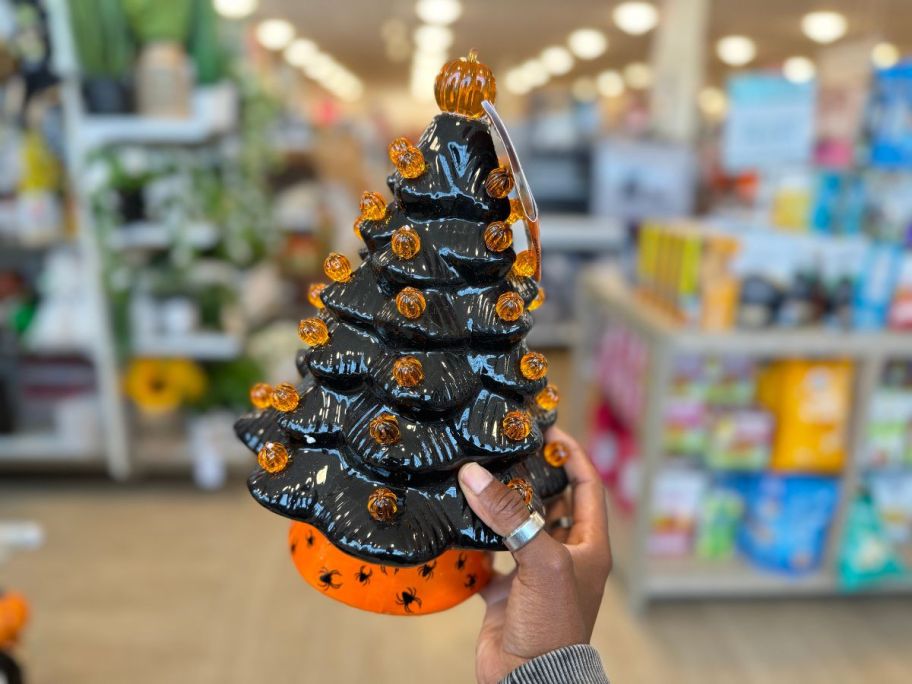 a womans hand holding a ceramic lighted halloween tree