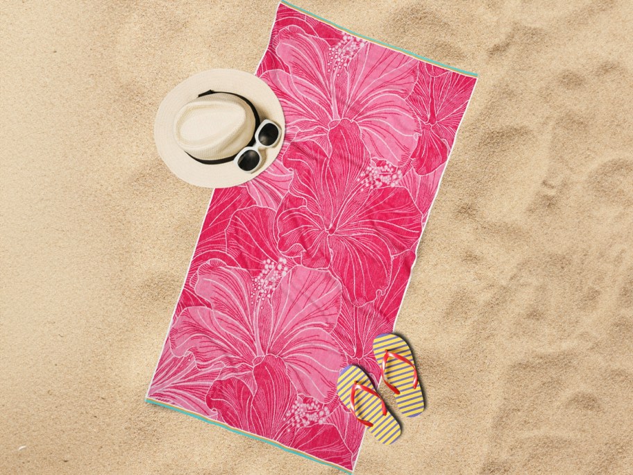 pink beach towel laying in sand with hat 