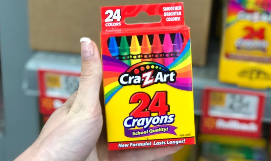 a womans hand holding a 24 count pack of crayons