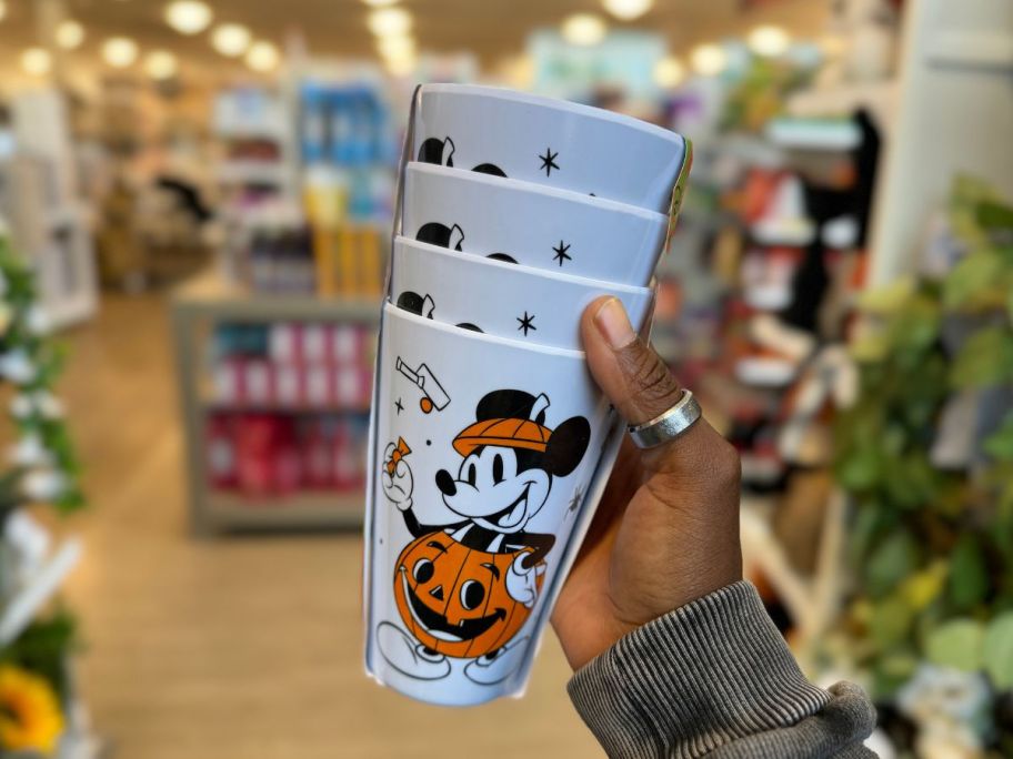 a womans hand holding a 4 pack of mickey mouse halloween cups