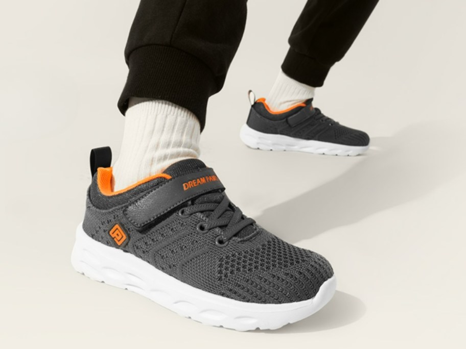 little boys feet wearing grey slip on sneakers with orange accents