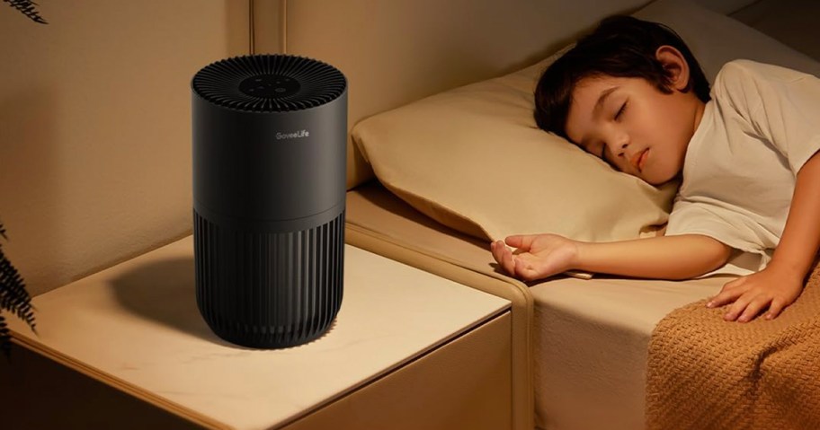 black air purifier on side table next to child sleeping in bed