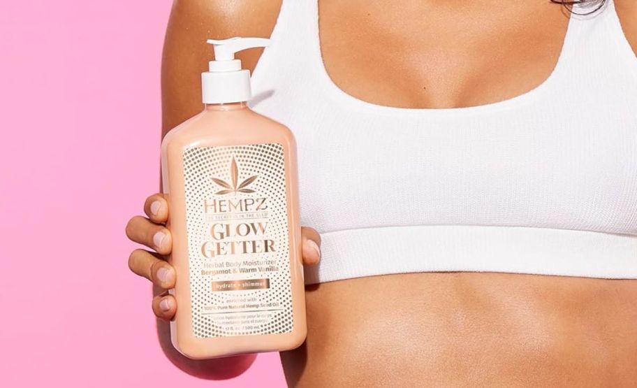 a womans hand holding a bottle of hempz glow getter shimmer body moisturzer