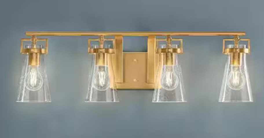gold brass 4 light vanity light with glass shades on a blue wall