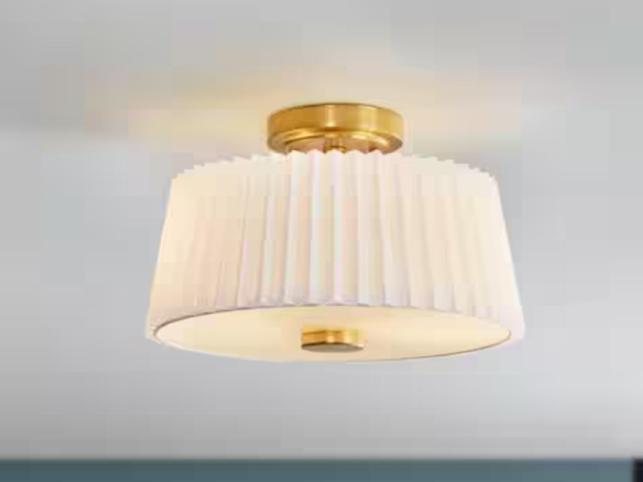flush ceiling light with gold accents and white pleated fabric shade on a ceiling