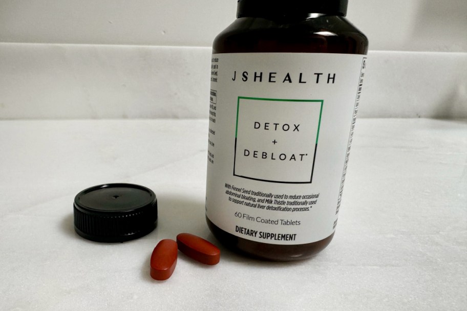 bottle of jshealth detox and debloat supplements with two pills sitting next to it on a counter
