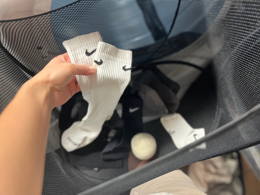 hand holding two white nike socks in mesh laundry basket